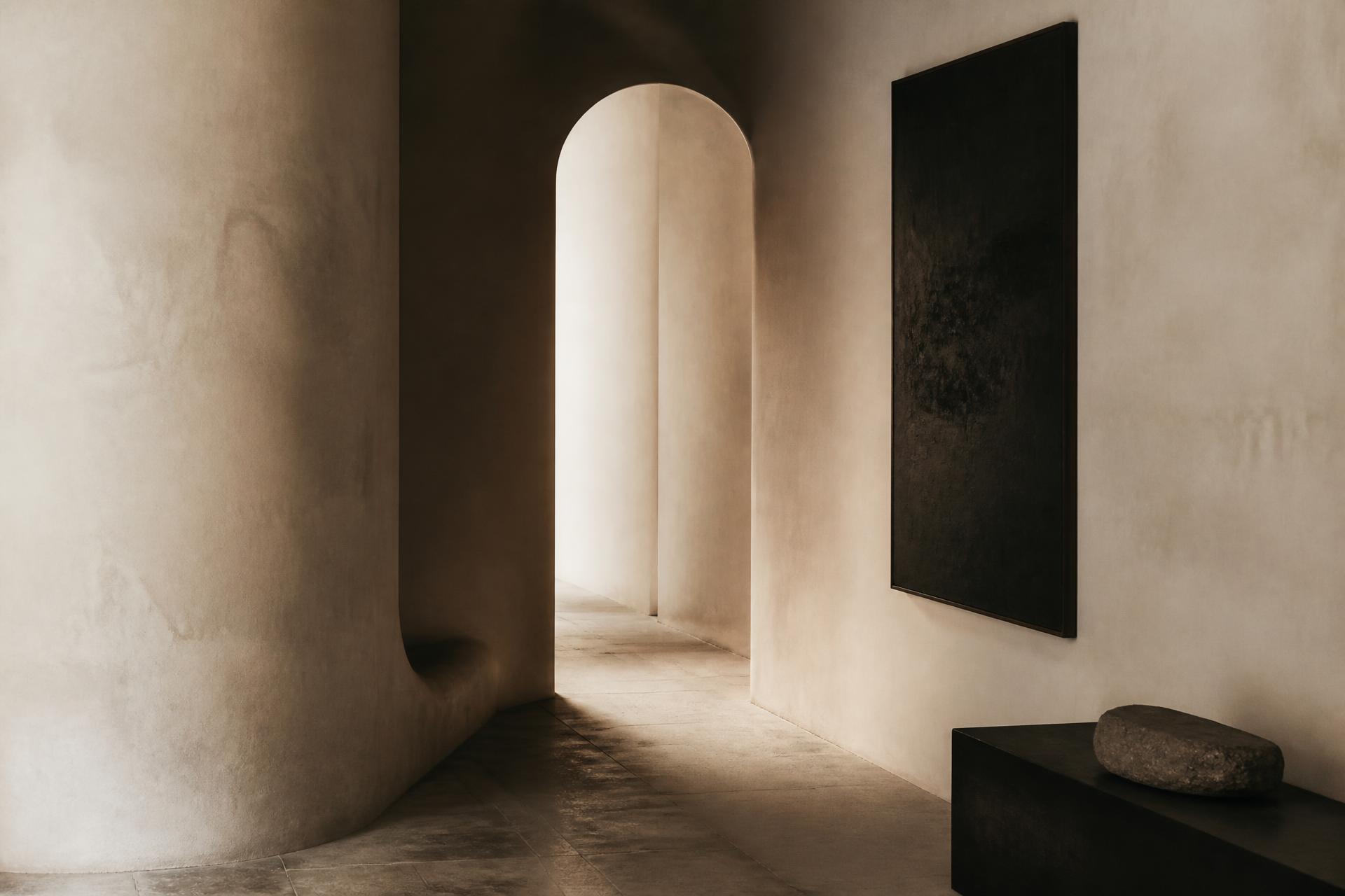 Minimal ivory-plaster corridor with raking daylight and a single dark canvas