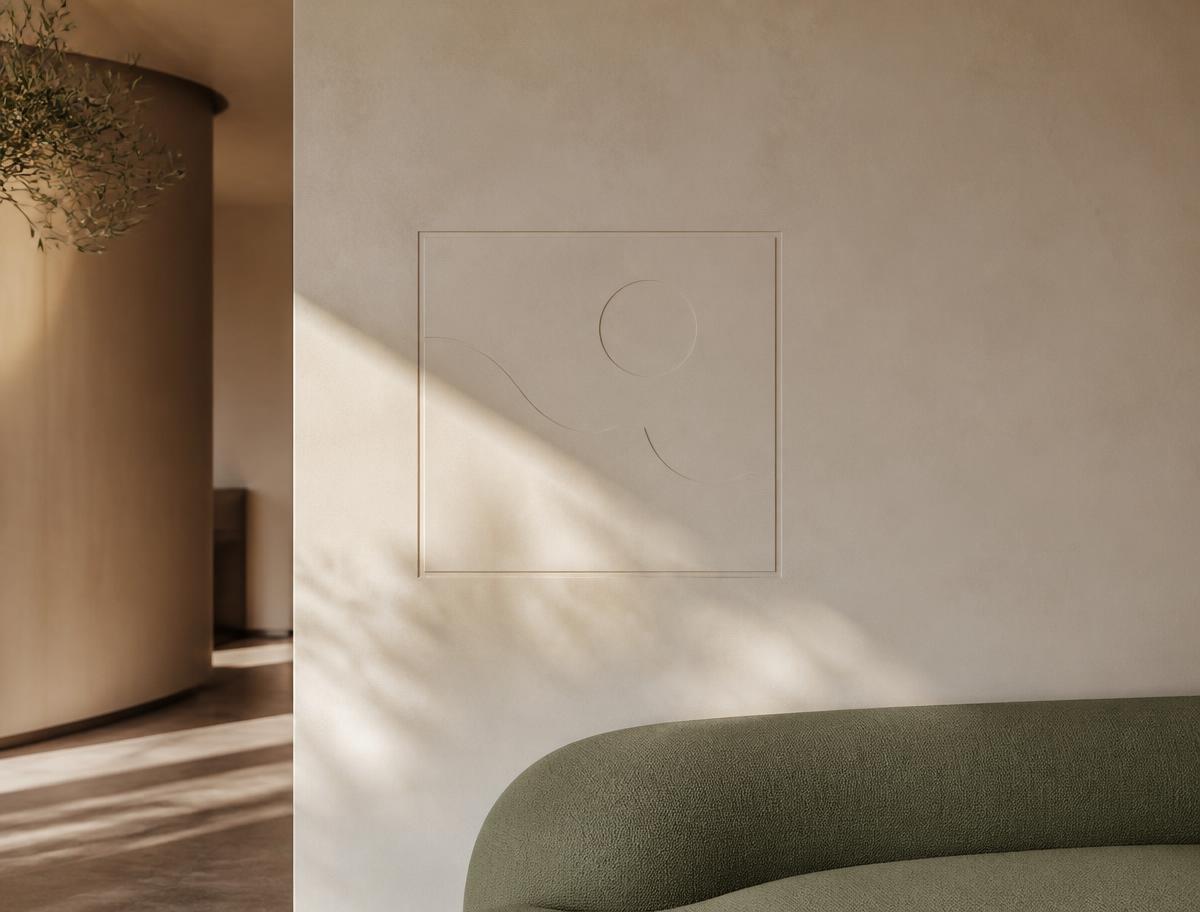 Minimal hospitality interior: an ivory plaster wall with a blind-debossed signage panel, dappled daylight and the edge of sage linen seating